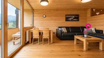 Helles Wohn- und Esszimmer mit Holzelementen und Zugang zum Balkon mit Bergblick.