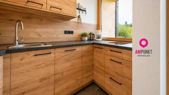 Funktionale Küche mit Holzfronten, dunkler Arbeitsplatte und Fenster mit Blick ins Grüne.