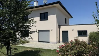 Modernes Einfamilienhaus mit heller Fassade, Garage und gepflegtem Vorgarten unter blauem Himmel.