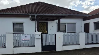 Einfamilienhaus mit weißer Fassade, Satteldach und integrierter Garage, umgeben von einem gepflegten Vorgarten.