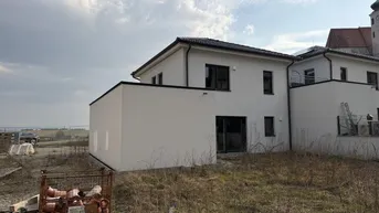 Rückseite eines Neubauhauses mit Blick auf eine Kirche und die umliegende Landschaft.