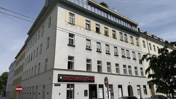 Mehrstöckiges Gebäude mit moderner Dachaufstockung und Geschäften im Erdgeschoss an einer Stadtstraße.