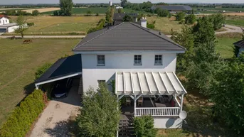 Luftaufnahme eines Einfamilienhauses mit Carport und Terrasse in ländlicher Umgebung.