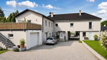 Großes Wohnhaus mit Garage, Balkon und gepflegter Kiesauffahrt unter blauem Himmel.