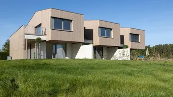Moderne Reihenhäuser mit Holzfassade und großzügiger Grünfläche in ländlicher Umgebung.