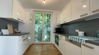 Moderne Küche mit weißen Hochglanzschränken, grauen Arbeitsplatten und Zugang zum Außenbereich.