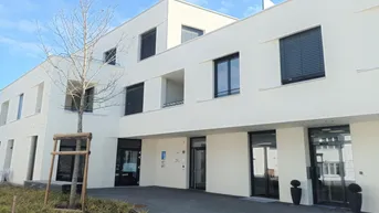 Modernes Mehrfamilienhaus mit weißer Fassade und dunklen Fensterläden unter blauem Himmel.