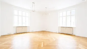Heller, leerer Wohnraum mit Fischgrätparkett, zwei großen Fenstern und viel natürlichem Licht.