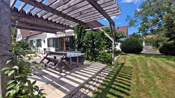 Sonniger Terrassenbereich mit Holzpergola und Sitzgelegenheiten im Grünen.