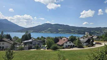 Panoramablick auf einen malerischen See, umgeben von Bergen und einer charmanten Siedlung.