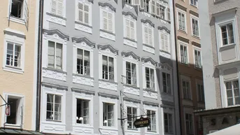 Historisches Gebäude mit aufwendig gestalteter Fassade, vielen Fenstern und traditionellen Fensterläden in einer belebten Stadtstraße.