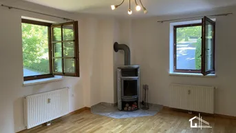 Heller Wohnraum mit Holzboden, zwei Fenstern und einem gemütlichen Holzofen.