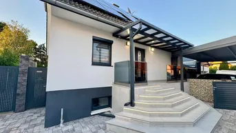 Modernes Einfamilienhaus mit Photovoltaikanlage auf dem Dach und beleuchtetem Eingangsbereich.