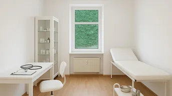 Helles Behandlungszimmer mit Untersuchungsliege, Schreibtisch und Blick ins Grüne.