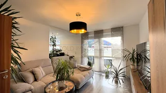 Helles Wohnzimmer mit modernem Sofa, Holzboden und Blick ins Grüne durch das Fenster.