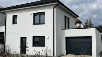 Neubau-Einfamilienhaus mit weißer Fassade, dunklen Fenstern und integrierter Garage.