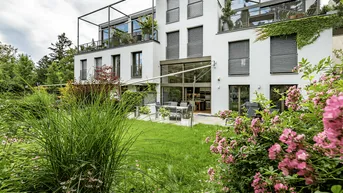 Moderne Wohnanlage mit weißer Fassade, großen Fenstern und gepflegtem Gartenbereich mit Terrasse.