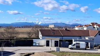Weitblick über die Landschaft mit Häusern und schneebedeckten Bergen im Hintergrund.