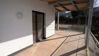 Großer, gefliester Balkon mit Glasgeländer und Blick auf die grüne Umgebung.