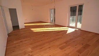 Helles, leeres Wohnzimmer mit Holzboden und Zugang zu einem Balkon, durchflutet von Sonnenlicht.
