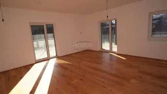 Helles, leeres Zimmer mit Holzboden und Zugang zu einem Balkon, durchflutet von Sonnenlicht.