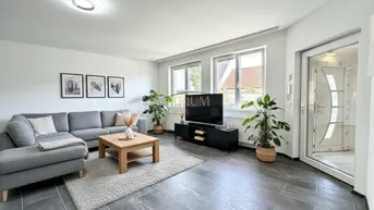 Helles Wohnzimmer mit modernem Sofa, Holztisch und dunklen Fliesen, durch große Fenster gut belichtet.