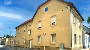 Gebäudeansicht eines älteren Mehrfamilienhauses mit gelber Fassade und Fenstern zur Straße hin.