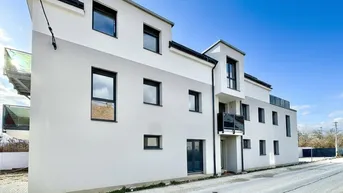 Modernes Mehrfamilienhaus mit weißer und grauer Fassade unter blauem Himmel.