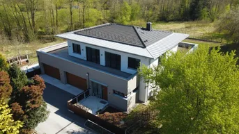 Luftaufnahme eines modernen Einfamilienhauses mit Satteldach und Photovoltaikanlage in grüner Umgebung.