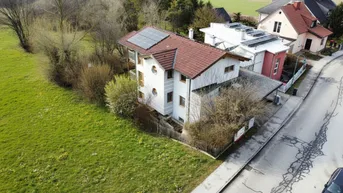 Luftaufnahme des Hauses mit Solaranlage auf dem Dach, umgeben von grünen Feldern und einer Straße.