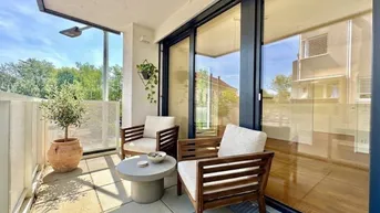 Heller Balkon mit modernen Holzmöbeln, Fliesenboden und Blick ins Grüne.