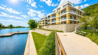 Modernes Wohngebäude am Wasser mit Balkonen und Blick auf den See unter blauem Himmel.