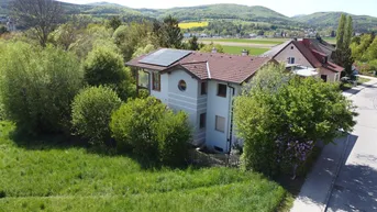 Freistehendes Haus mit Ziegeldach und Photovoltaikanlage, umgeben von viel Grün und Hügellandschaft.