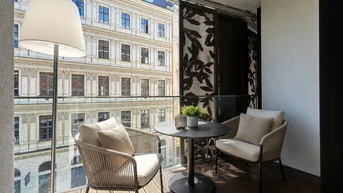Gemütlicher Balkon mit Holzboden und Sitzgelegenheiten, mit Blick auf die gegenüberliegenden Gebäude.