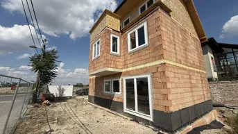 Neubau eines Einfamilienhauses im Rohbauzustand mit sichtbaren Ziegelwänden und Fenstern.