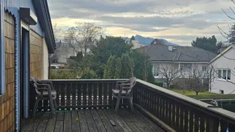 Großer Holzbalkon mit Geländer und Blick auf die umliegende Landschaft und Berge.