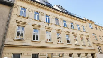 Altbau-Fassade mit mehreren Stockwerken und Dachfenstern unter blauem Himmel.