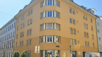 Eckgebäude mit gelber Fassade und großen Fenstern an einer städtischen Straße.