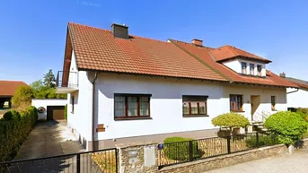 Gut gepflegtes Einfamilienhaus mit weißer Fassade, rotem Satteldach, Balkon und Garage.