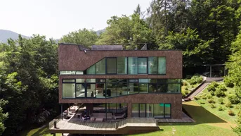 Modernes Wohnhaus mit großer Holzterrasse und weitläufigem Garten, umgeben von üppiger Natur.