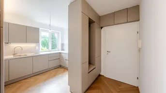 Moderne Küche mit beigefarbenen Schränken, Holzboden und integriertem Garderobenbereich.