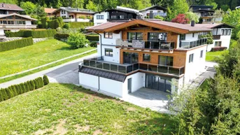 Modernes Chalet mit Holzfassade, mehreren Balkonen und einer Terrasse, umgeben von grüner Natur.
