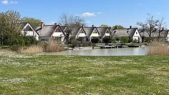 Reihen von Häusern am Wasser mit grüner Wiese unter einem klaren blauen Himmel.