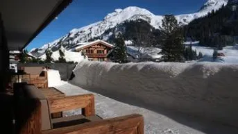 Balkon mit Holzbänken, umgeben von Schnee und Panoramablick auf die verschneiten Berge.