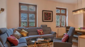 Gemütlicher Wohn- und Essbereich mit bequemer Sitzecke, Holzboden und Bergblick durch die Fenster.