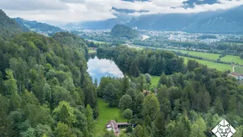 Panoramablick auf die Berglandschaft mit See und einem Haus inmitten grüner Wälder.