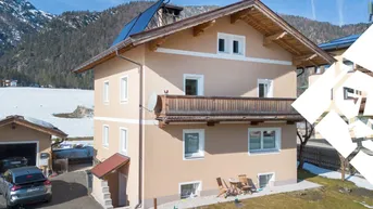 Traditionelles Haus mit Balkon und Solaranlage vor alpiner Bergkulisse im Winter.