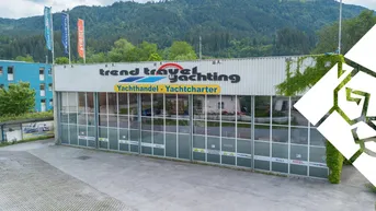 Ansicht des Geschäftsgebäudes mit großer Glasfassade und Beschilderung, umgeben von Bergen und einem Parkplatz.
