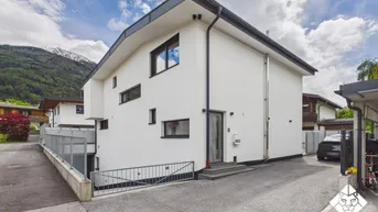 Moderne Architektur mit weißer Fassade und Zufahrt, umgeben von einer bergigen Landschaft.