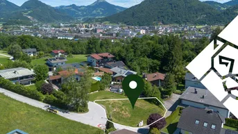 Luftaufnahme eines Baugrundstücks mit umliegenden Häusern und Bergpanorama im Hintergrund.